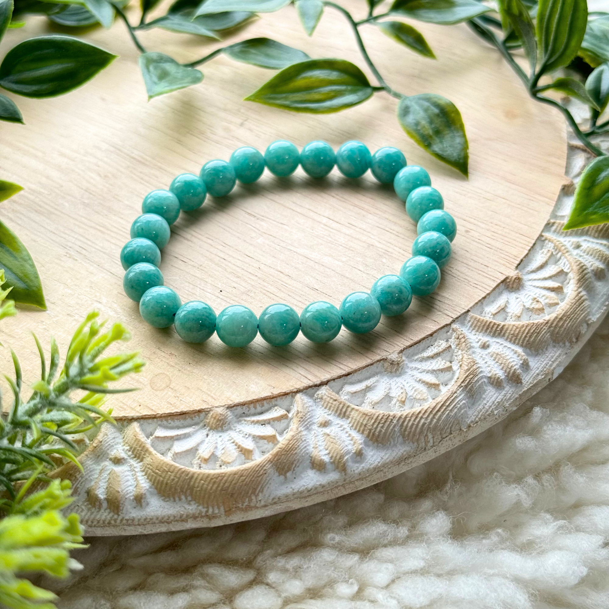 Turquoise bead bracelet on a decorative wooden plate with greenery.